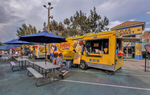 couple seated at picnic table near yellow vendor trailer at world food trucks kissimmee