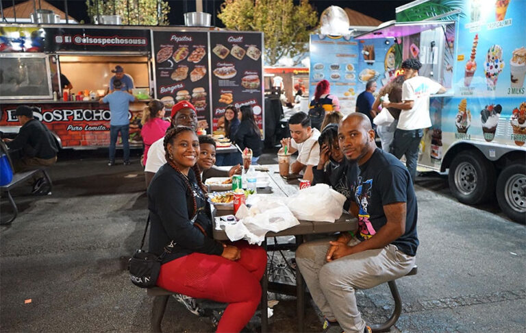 friends eating at table in outdoor area between food trucks at world food trucks kissimmee