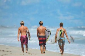 three teens carrying surf boards down the beach at space coast beaches