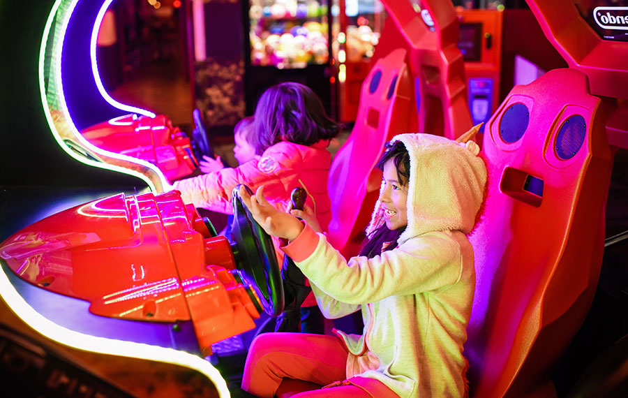 girl and other kids playing race car driving video game at arcade center