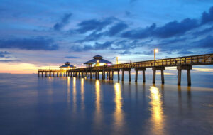 lighted fishing pier with blue and gold sunset through clouds with long exposure glassy sea fort myers