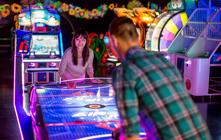 man and woman playing air hockey in colorful arcade with black light