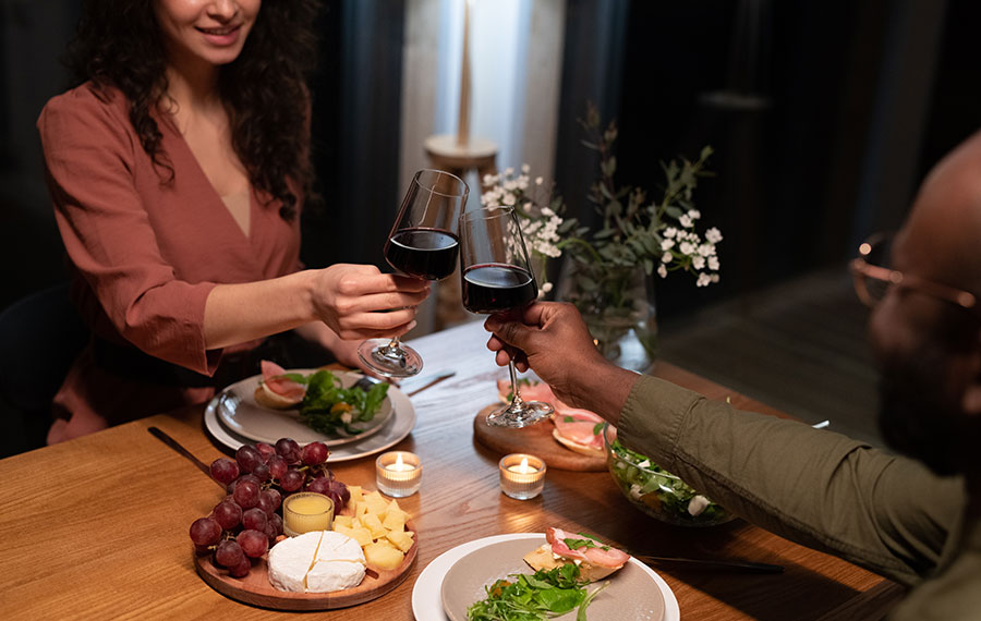 man and woman toasting red wine over dinner table in romantic restaurant setting