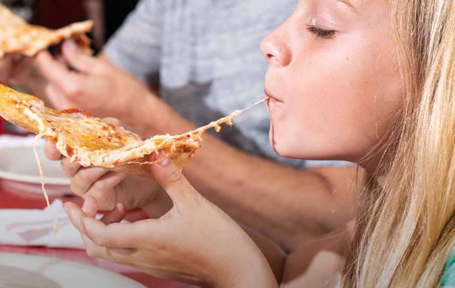 young blonde girl biting into pizza slice close up