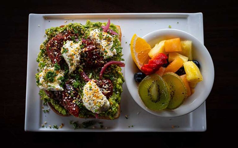 avocado toast with eggs and fruit salad on rectangular plate at polonza bistro pensacola