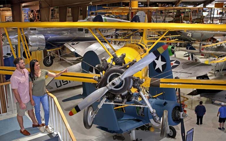 couple looking at yellow biplane suspended in hangar with many planes at national naval aviation museum pensacola
