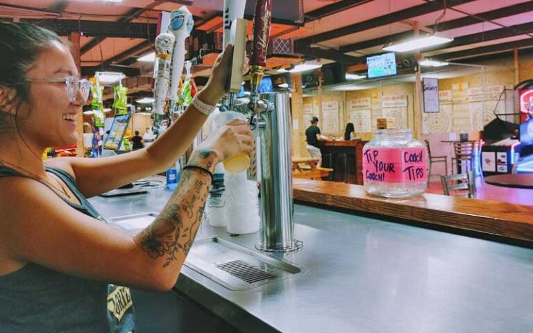 girl serving beer on taps with arcade games and axe targets at grizzly axes pensacola