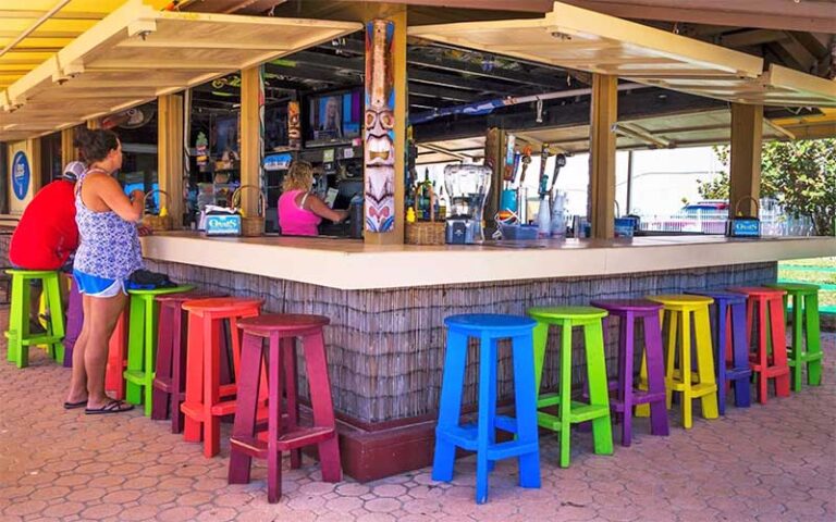 outdoor tiki themed bar with lifted shudders and colorful stools at fountain beach resort daytona