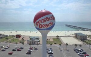 water tower with beach ball design and coast with pier in background at pensacola beach