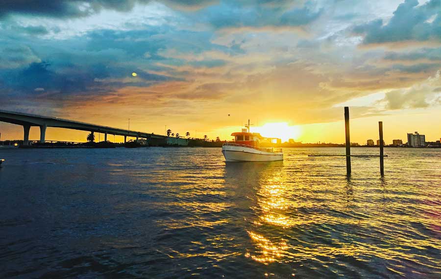 boat on bay with sunset behind yellow on blue cloudy sky and bridge little toot dolphin adventure clearwater