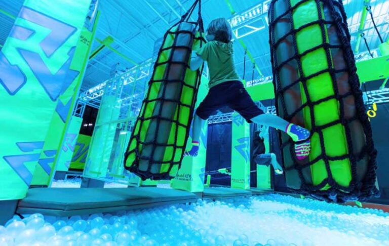 boy stretching to grab obstacle over ball pit at urban air trampoline adventure park