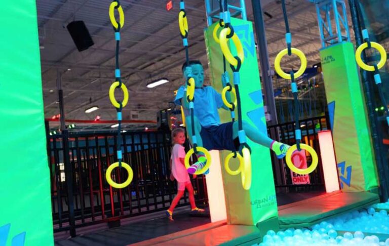 boy swinging from rings with blacklit obstacle course at urban air trampoline adventure park