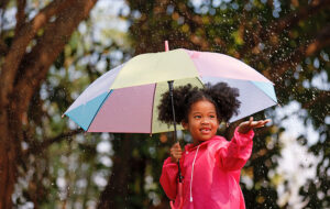 little girl wearing magenta raincoat with rainbow umbrella and hand out for rain