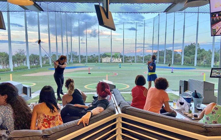 two golfers swinging in separate bays with seating at drive shack west palm beach