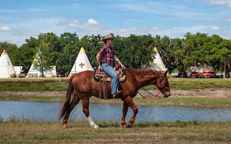 woman riding horse with teepees and lake at westgate river ranch resort rodeo