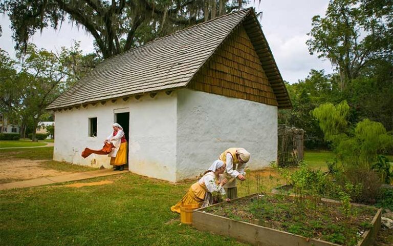 women in period costume gardening near modest house at mission san luis tallahassee