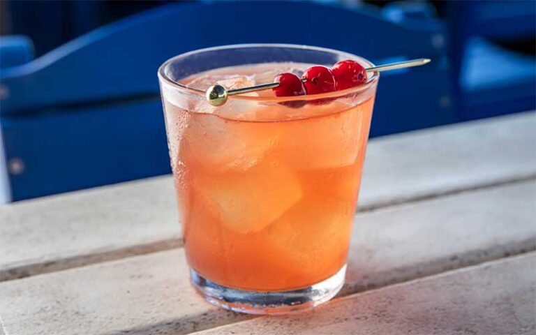 cocktail with orange color garnished with cherries on outdoor table at sandbar amelia island fernandina beach