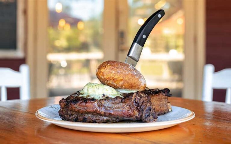 large steak with roll and knife on outdoor table at marche burette omni amelia island