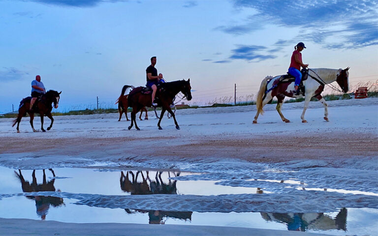 three horseback riders at dusk riding along beach at amelia island horseback riding