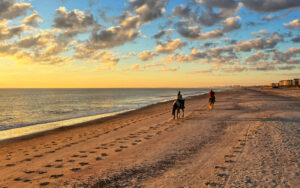 two horseback riders on beach with sunset at amelia island horseback riding