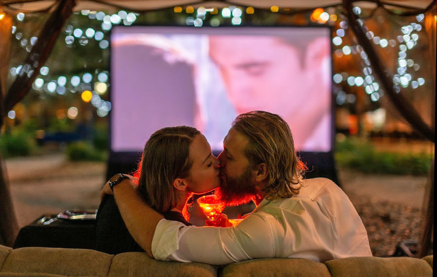 couple kissing seated on sofa with movie playing on screen outdoors tallahassee date night