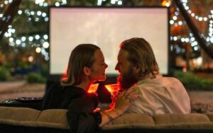 couple smiling sitting close on couch with movie and drinks outside at tallahassee date night