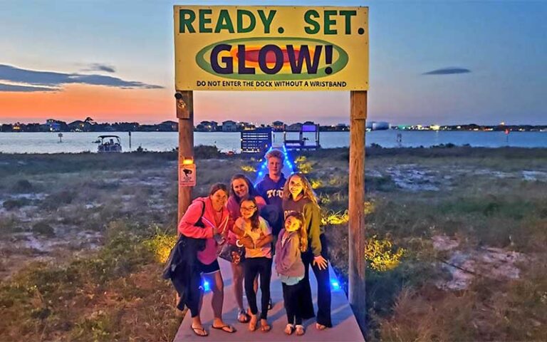 family under boardwalk sign with beach sunset background at glow paddle pensacola beach