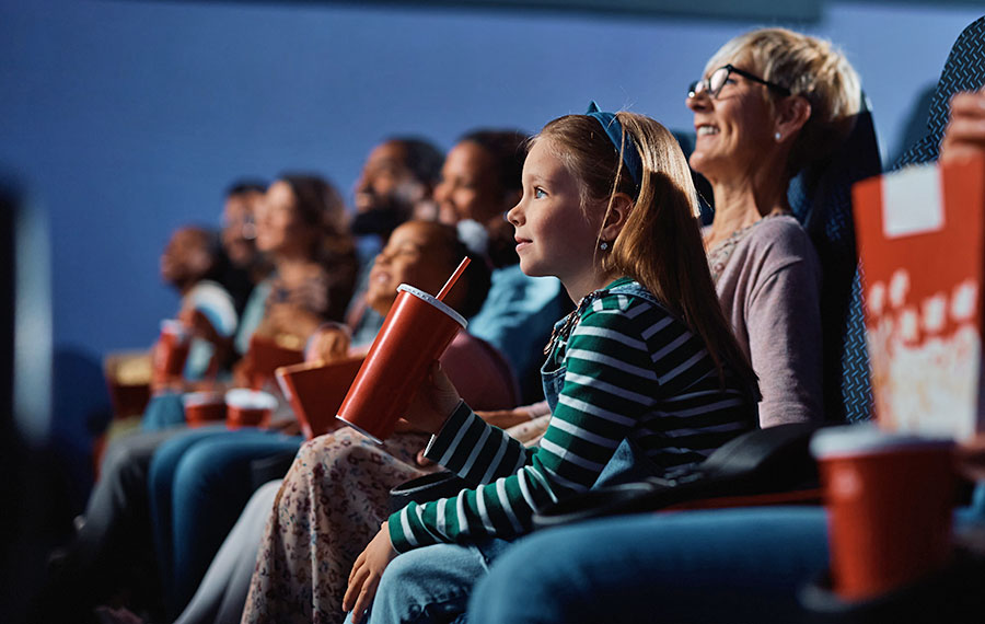 little girl drinking fountain drink watching movie with mom and others