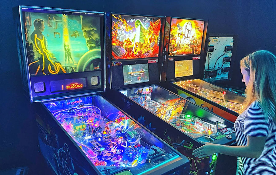 row of pinball machines with girl playing at the grid arcade pensacola