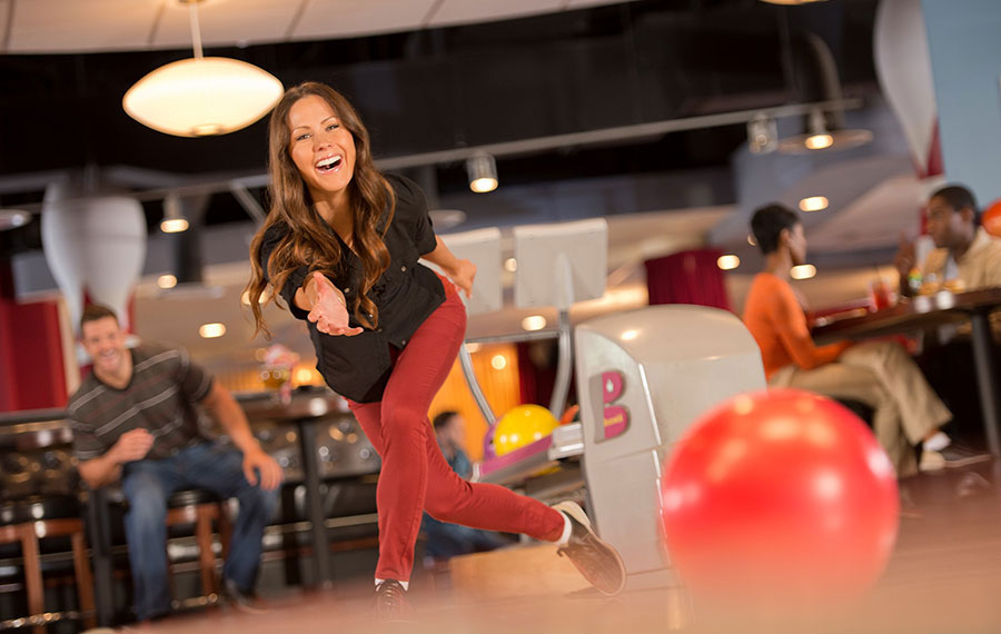 smiling woman bowling while man waits his turn in colorful bowling alley