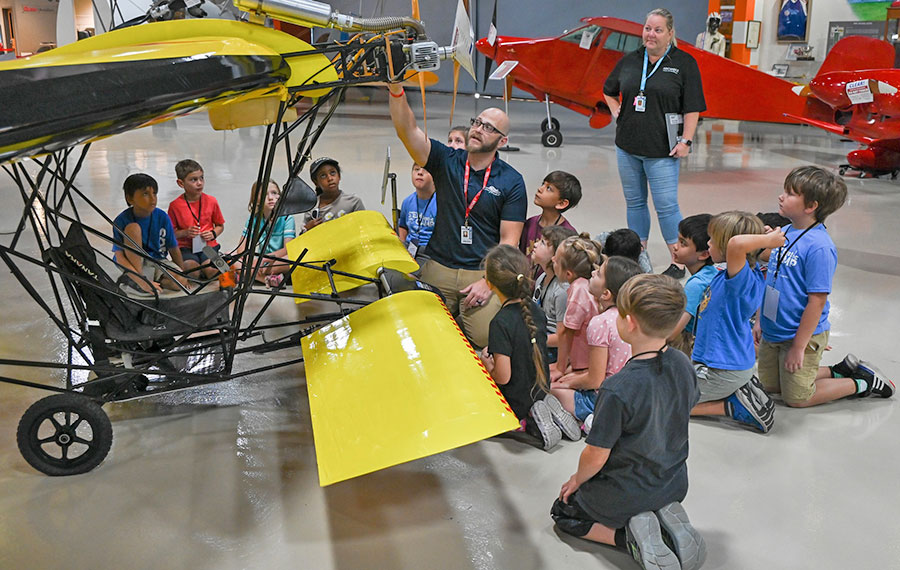 tour group of children gathered around yellow aircraft listening to tour guide at florida air museum lakeland