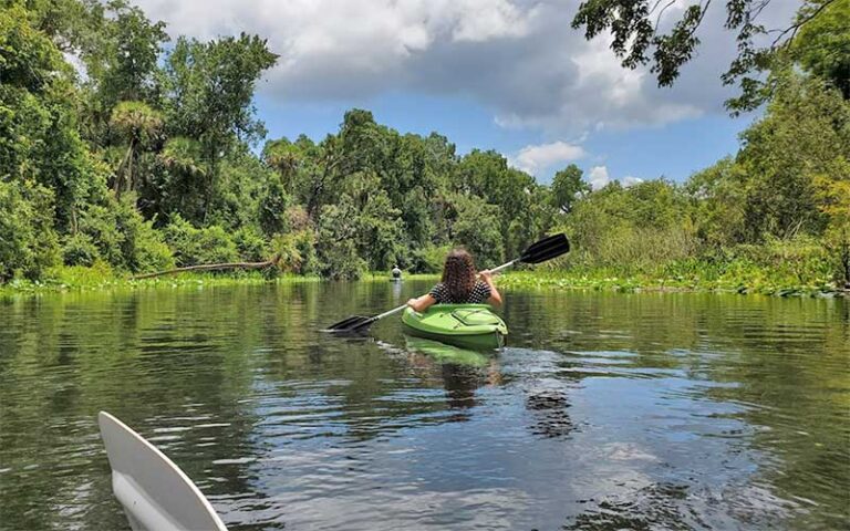 woman in green kayak paddling river with dense foliage at ocala national forest