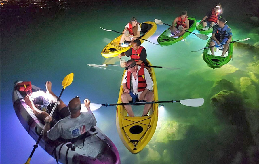 colorful kayaks with riders paddling over lighted bay at night sarasota