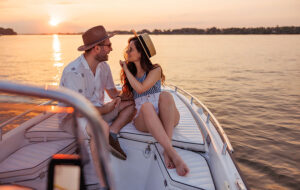 couple smiling and talking on private boat adrift on bay with sunset over barrier island