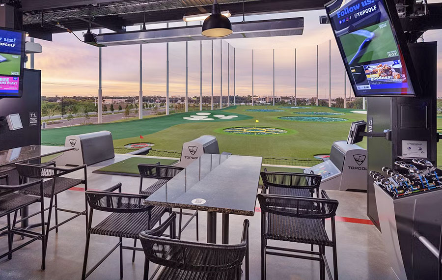 driving range bay with seating and screens overlooking field of targets at dusk topgolf fort myers