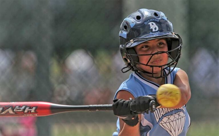 helmeted girl swinging at softball in batting cage at adventure landing st augustine