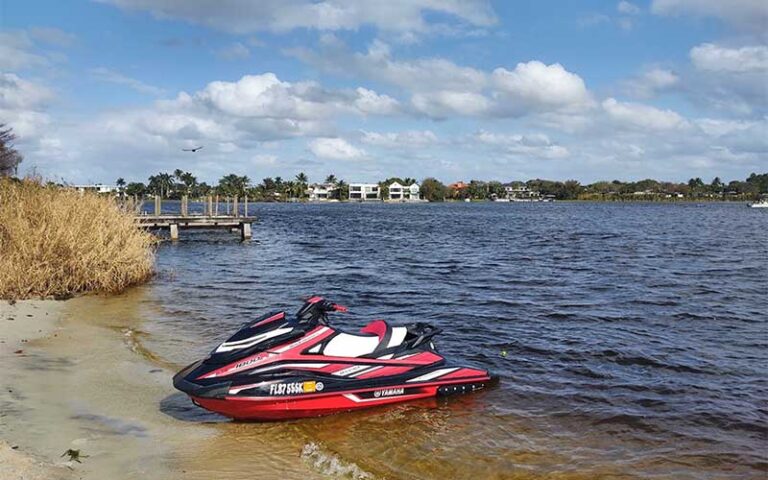 red jet ski on beach of lake with pier and houses at lake ida west park delray beach