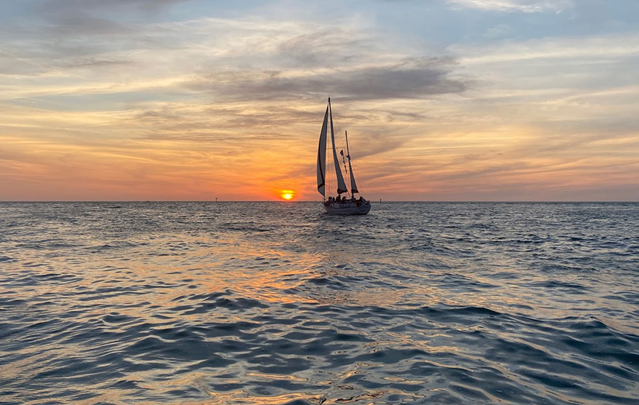 sailboat silhouetted on open water with sunset behind and clouded orange and blue sky dolphin landings charter boats clearwater tampa