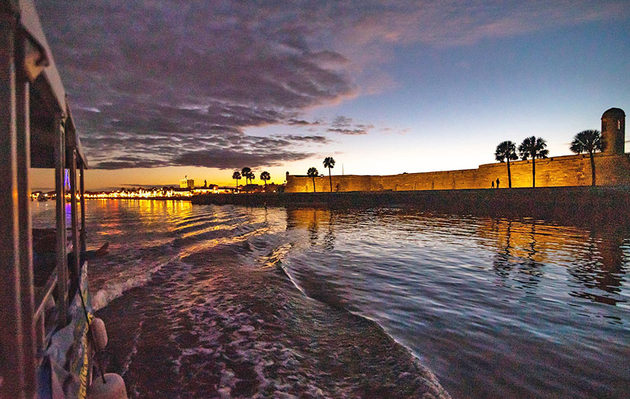 view from tour boat of castillo de san marcos with lighted skyline with clouded sunset st augustine