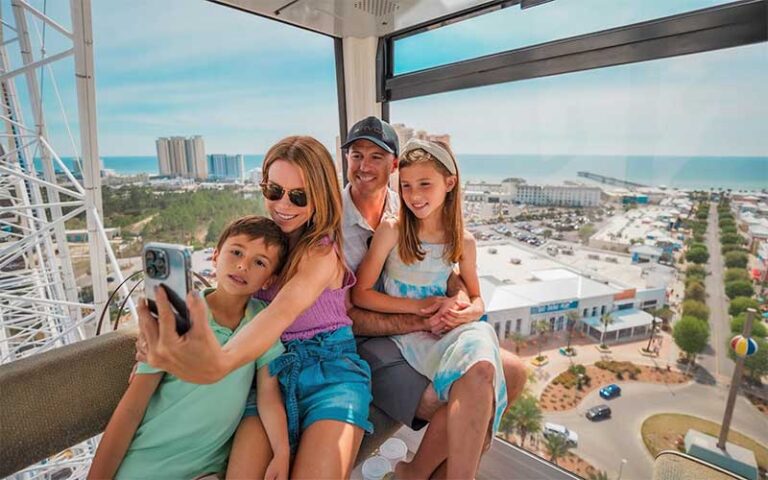 family of four taking selfie in gondola with park view at skywheel at pier park panama city beach