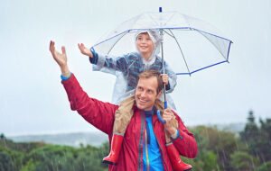 father carrying son on shoulders with umbrella in outdoor rain