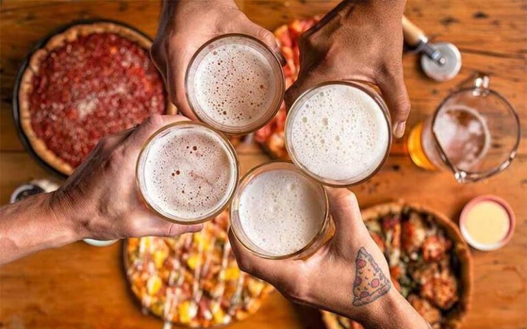 hands toasting beer pints over pizzas on table at uno pizzeria grill orlando kissimmee