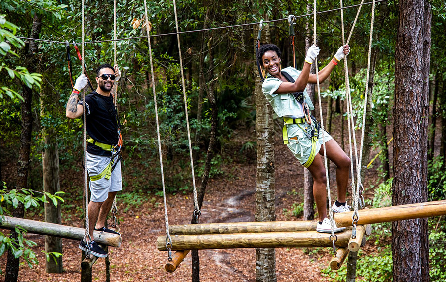 man and woman on log ropes course in forest area at orlando tree trek