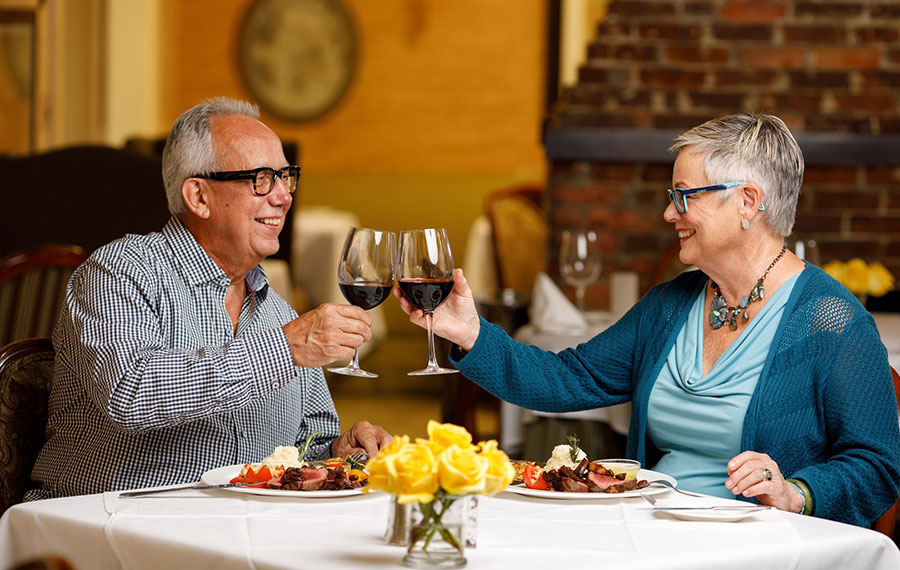 senior couple toasting wine over elegant dinners at restaurant table