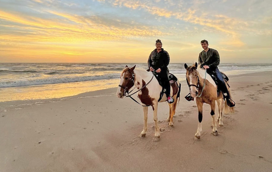 smiling couple riding on horses on beach with sunrise sky at amelia island horseback riding