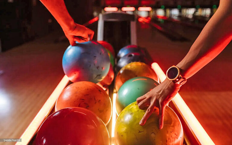 two hands reaching for bowling balls on rack at bowlero west ocala