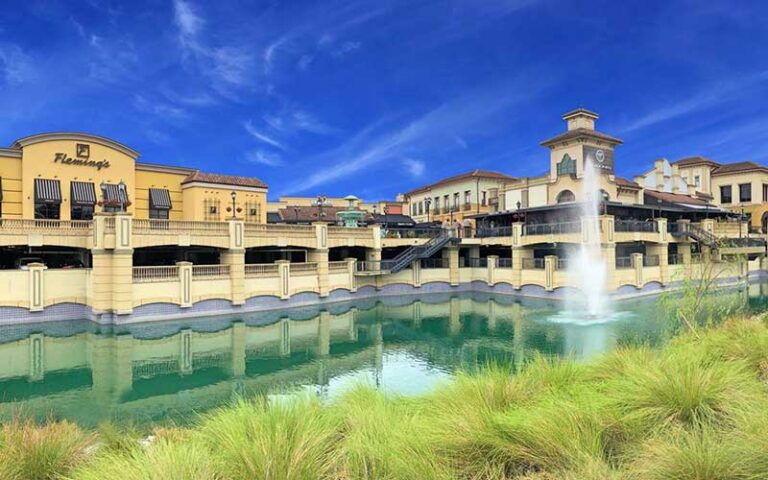 view from grass of lake with fountain and restaurants at dellagio town center orlando