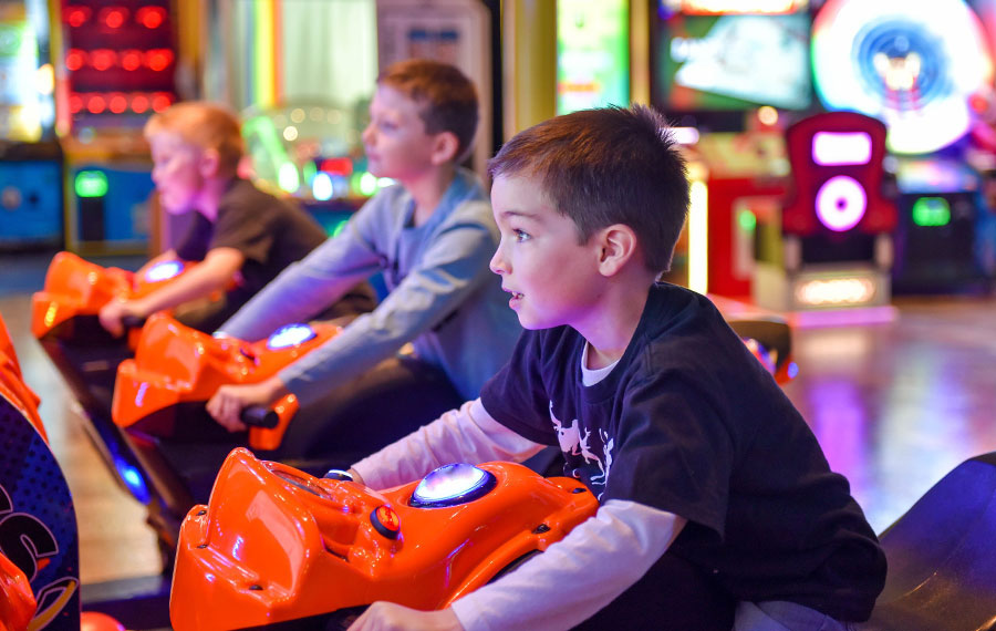 young boys competing on motorcycle racing game at arcade