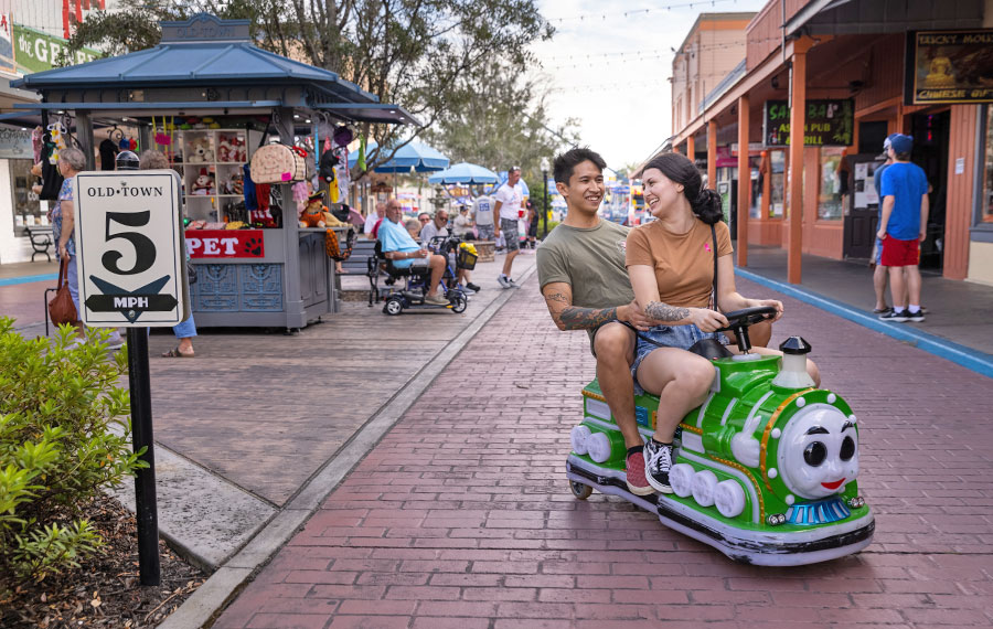 young couple laughing while riding train ride at outdoor street area with five mph sign at old town kissimmee