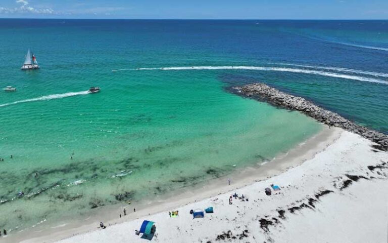 aerial view of beach with rock jetty and boats over green water at adventures at sea panama city beach